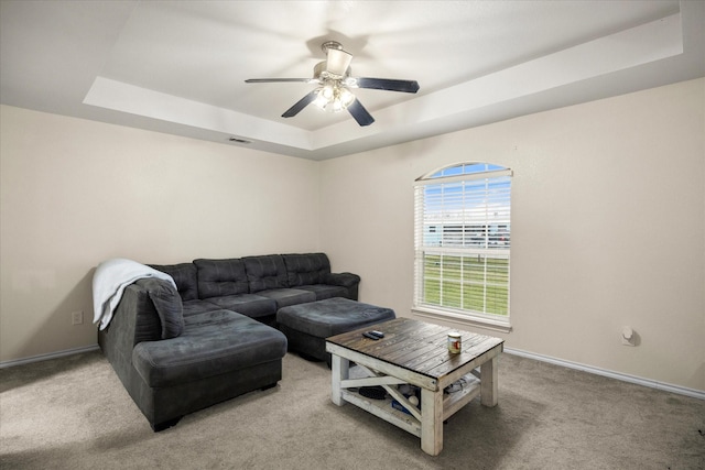 living area with light carpet, visible vents, baseboards, a raised ceiling, and a ceiling fan