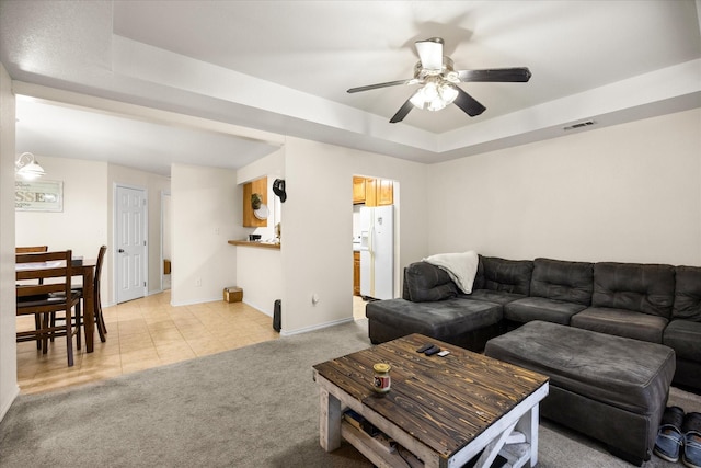 living room featuring light carpet, baseboards, visible vents, ceiling fan, and a tray ceiling