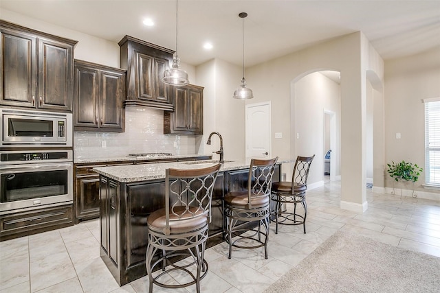 kitchen with arched walkways, a breakfast bar, appliances with stainless steel finishes, backsplash, and light stone countertops