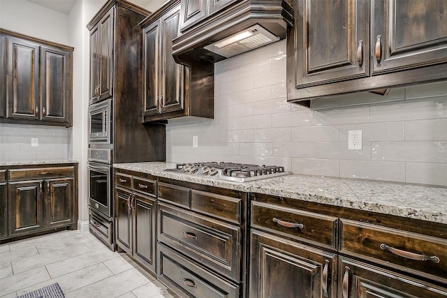 kitchen featuring appliances with stainless steel finishes, light stone countertops, custom exhaust hood, dark brown cabinets, and backsplash