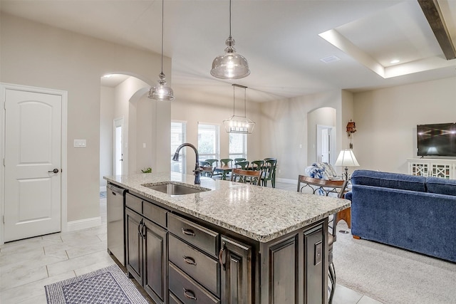 kitchen featuring light stone counters, arched walkways, stainless steel dishwasher, open floor plan, and a sink