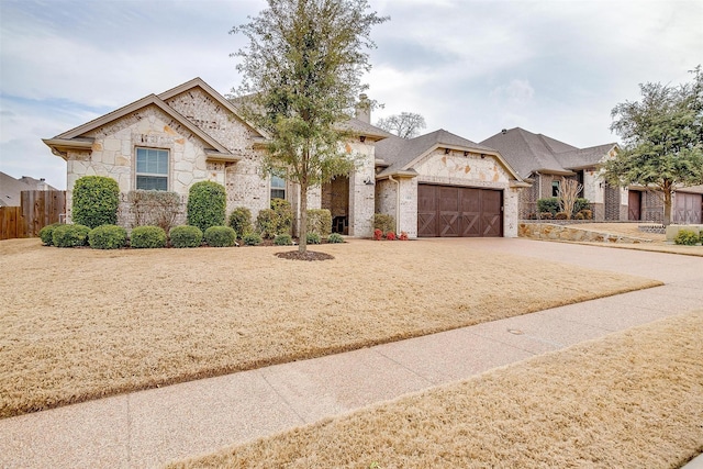 view of front facade with driveway, stone siding, a garage, and fence