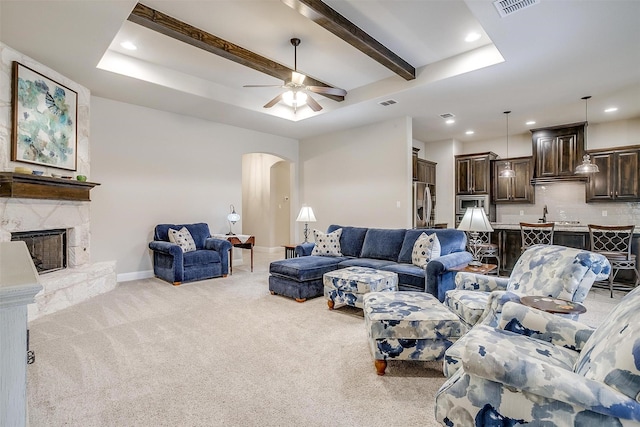 living area with arched walkways, a stone fireplace, light carpet, baseboards, and beam ceiling