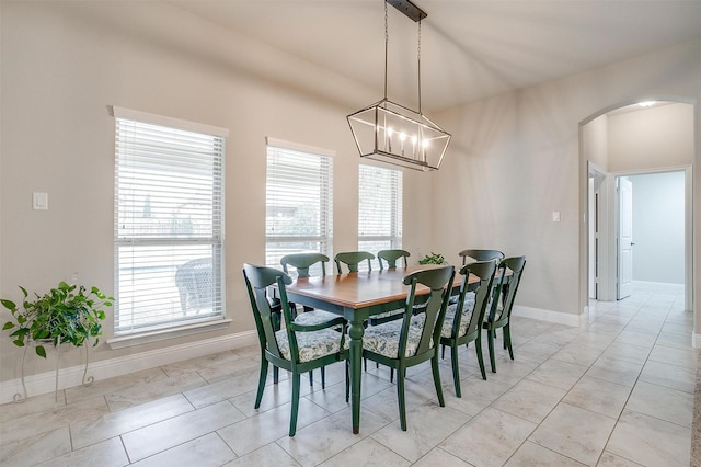 dining area with arched walkways, a notable chandelier, a wealth of natural light, and baseboards