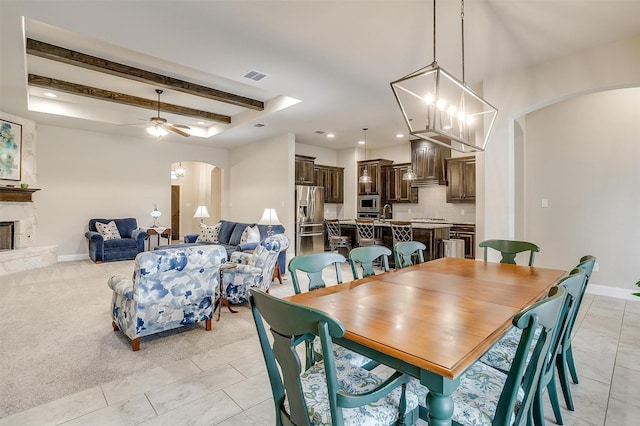 dining room with arched walkways, a raised ceiling, visible vents, a stone fireplace, and baseboards