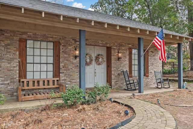 property entrance featuring a porch, brick siding, and a shingled roof