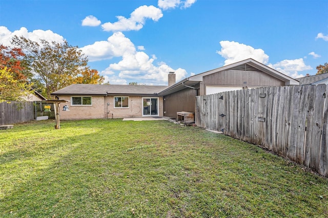 back of house with an attached garage, a fenced backyard, a lawn, a chimney, and a patio area