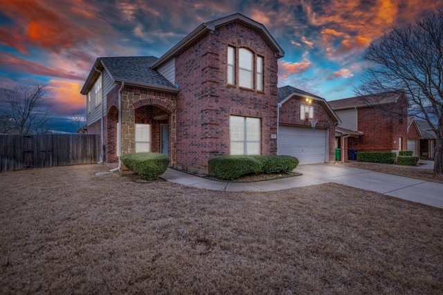 traditional-style home featuring fence, roof with shingles, an attached garage, concrete driveway, and brick siding