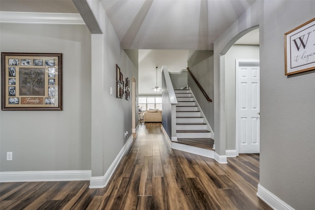 hallway with arched walkways, stairway, baseboards, and wood finished floors