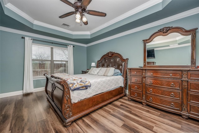 bedroom featuring visible vents, crown molding, baseboards, wood finished floors, and a raised ceiling