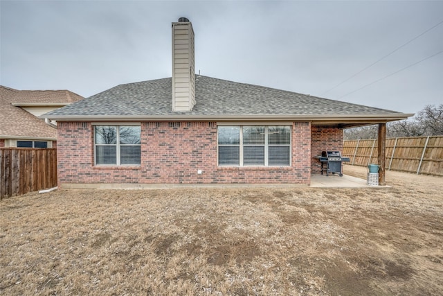 back of house featuring a patio, a fenced backyard, roof with shingles, brick siding, and a chimney