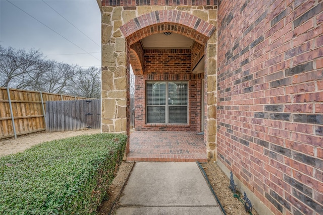 entrance to property with brick siding, stone siding, a patio area, and fence