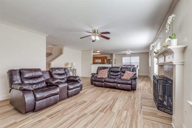 living area featuring light wood-type flooring, ceiling fan, baseboards, and a tile fireplace