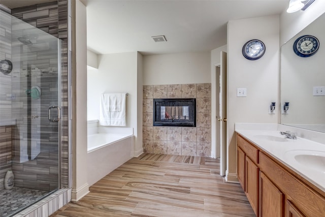 bathroom with a fireplace, a sink, visible vents, a bath, and a stall shower