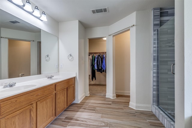 bathroom with double vanity, a shower stall, visible vents, and a walk in closet