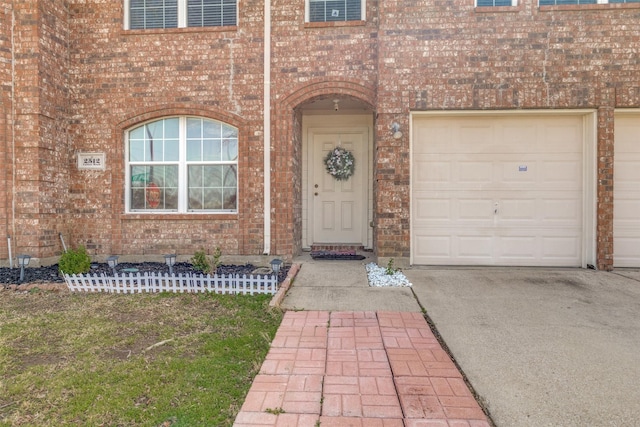 doorway to property featuring a garage, brick siding, and driveway