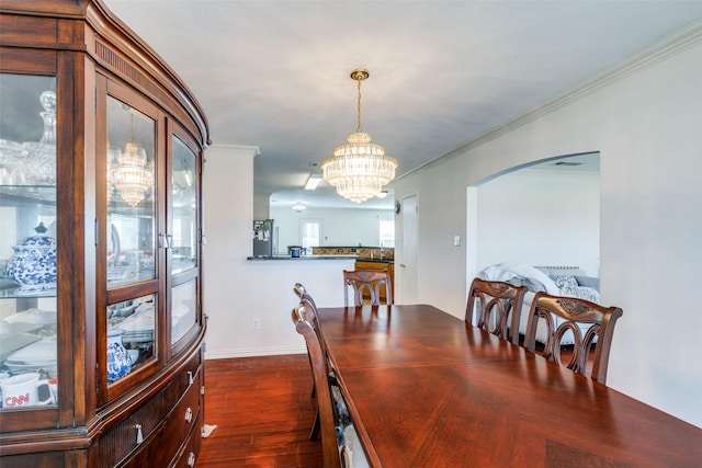 dining space featuring dark wood-style floors, an inviting chandelier, arched walkways, and crown molding