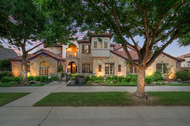 mediterranean / spanish home featuring a gate, stone siding, a balcony, and stucco siding