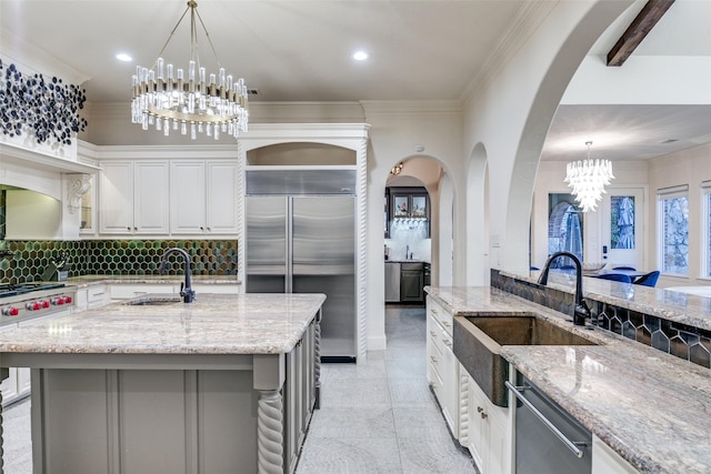 kitchen featuring tasteful backsplash, premium appliances, light stone counters, crown molding, and a sink