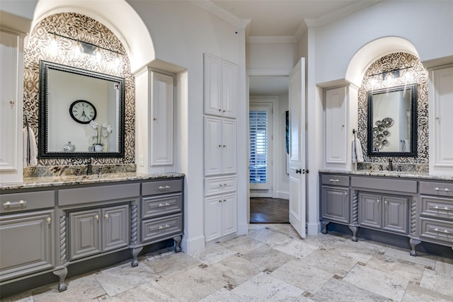 bathroom featuring crown molding, two vanities, a sink, and baseboards