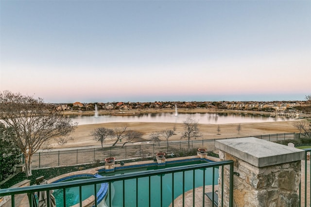 pool at dusk with a water view, fence, and a fenced in pool