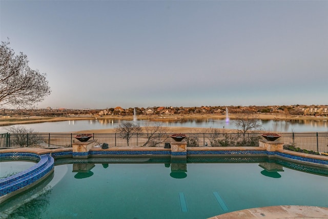 view of pool with a water view, a pool with connected hot tub, and fence