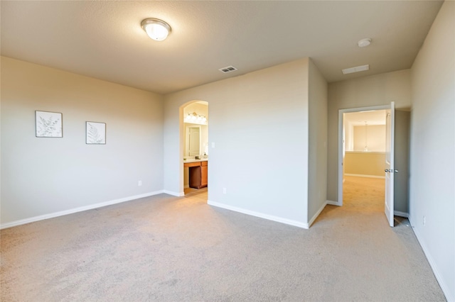 unfurnished bedroom with light colored carpet, arched walkways, visible vents, and baseboards