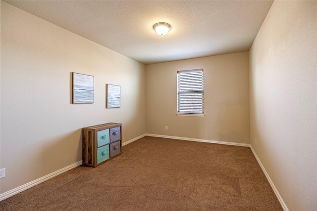 empty room with a textured ceiling, baseboards, and carpet flooring