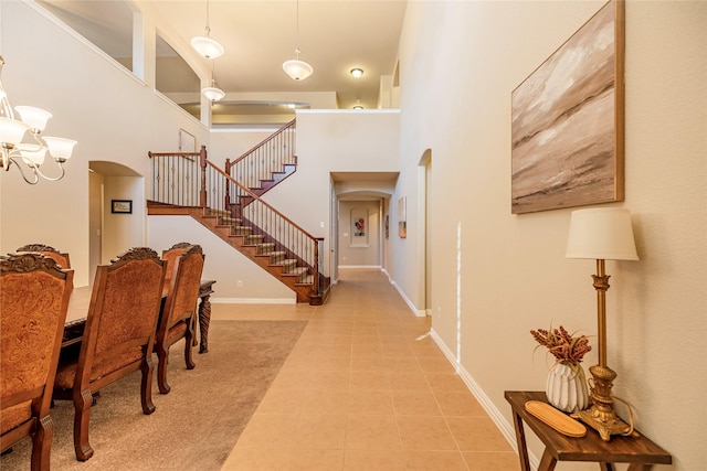 tiled foyer entrance with arched walkways, a notable chandelier, a towering ceiling, baseboards, and stairway