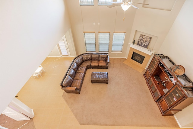 living room with a ceiling fan, a fireplace, a towering ceiling, and baseboards