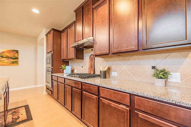 kitchen with under cabinet range hood, light stone counters, stainless steel appliances, and backsplash