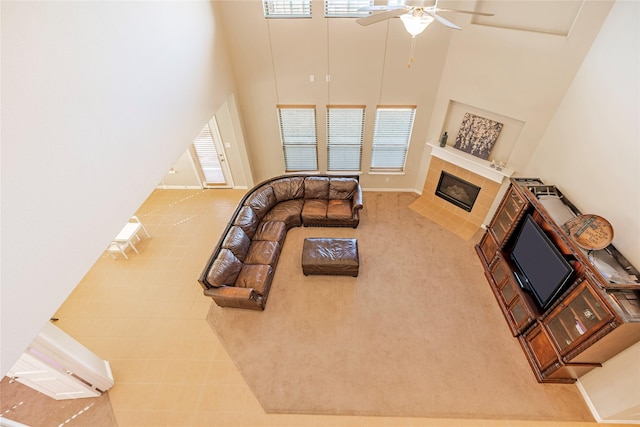 living area with a fireplace, a towering ceiling, baseboards, and ceiling fan