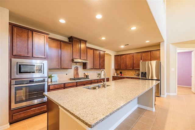 kitchen featuring under cabinet range hood, a sink, appliances with stainless steel finishes, tasteful backsplash, and an island with sink