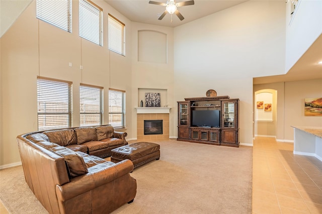 living room with a tile fireplace, baseboards, a ceiling fan, and light colored carpet