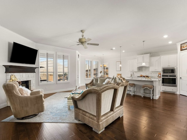 living room with crown molding, dark wood finished floors, a stone fireplace, and baseboards