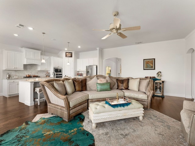 living area featuring dark wood-style floors, visible vents, arched walkways, and crown molding