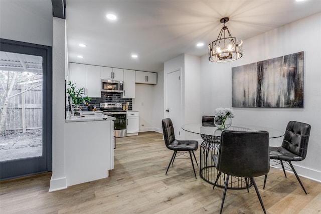 dining space featuring a chandelier, light wood-type flooring, baseboards, and recessed lighting