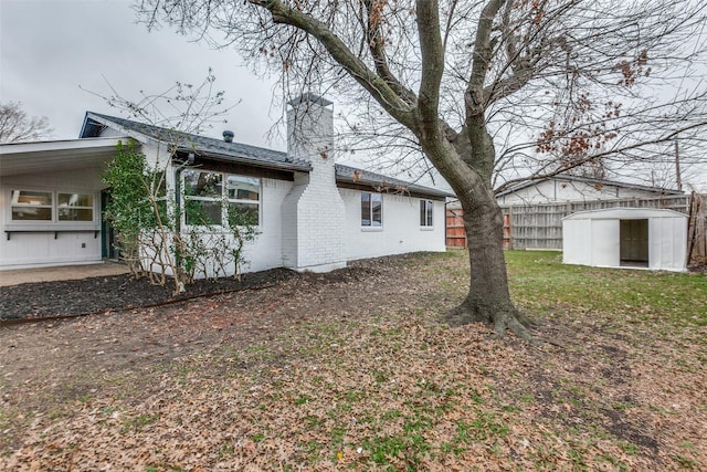 rear view of property featuring a storage shed, brick siding, an outdoor structure, fence, and a chimney