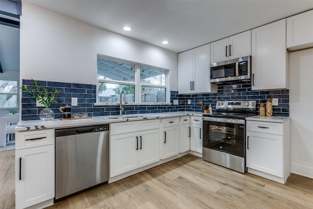 kitchen featuring stainless steel appliances, a sink, white cabinetry, decorative backsplash, and light wood finished floors