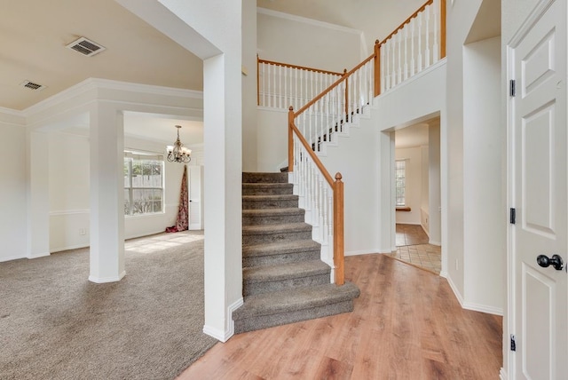 staircase with a chandelier, wood finished floors, visible vents, and crown molding