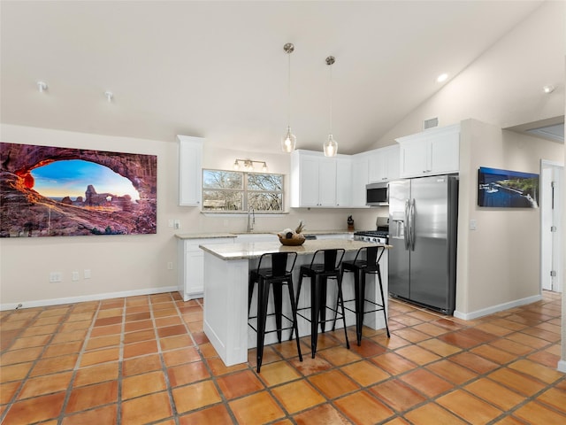 kitchen with light tile patterned floors, a kitchen island, appliances with stainless steel finishes, a breakfast bar area, and white cabinetry