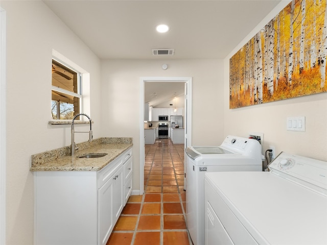 washroom with light tile patterned flooring, washing machine and dryer, a sink, visible vents, and cabinet space