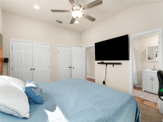 bedroom with lofted ceiling, ensuite bathroom, a sink, visible vents, and multiple closets