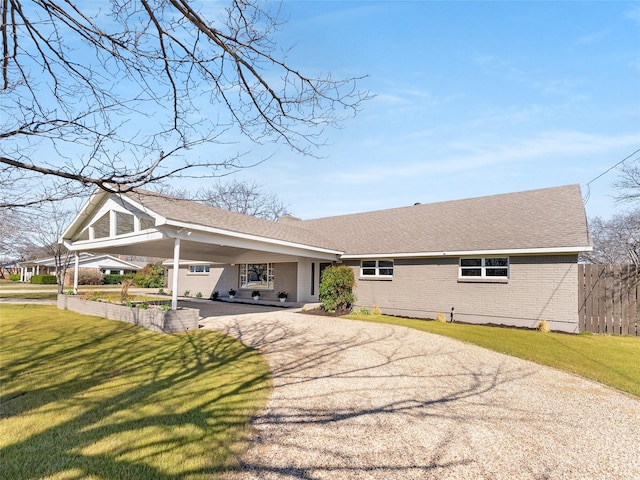 view of front of house featuring driveway, a shingled roof, an attached carport, a front lawn, and brick siding