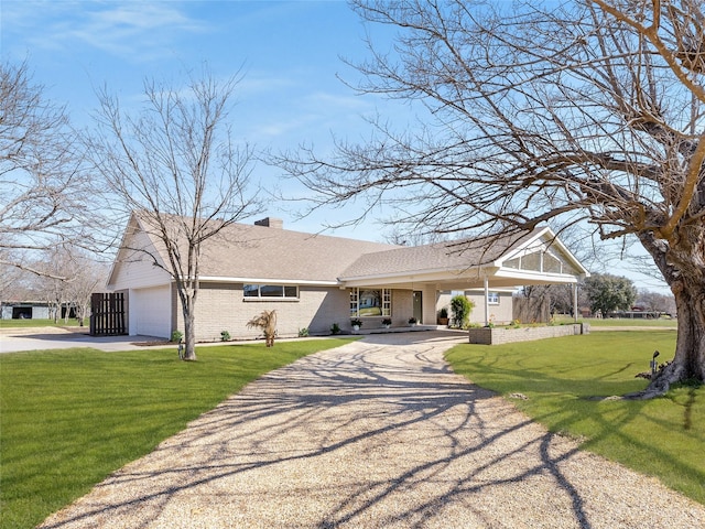 view of front of house with brick siding, a chimney, an attached garage, driveway, and a front lawn