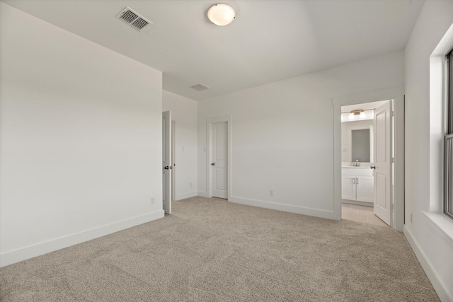 unfurnished bedroom with baseboards, visible vents, ensuite bathroom, and light colored carpet