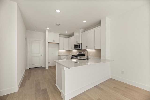 kitchen with light wood finished floors, visible vents, appliances with stainless steel finishes, a peninsula, and a sink