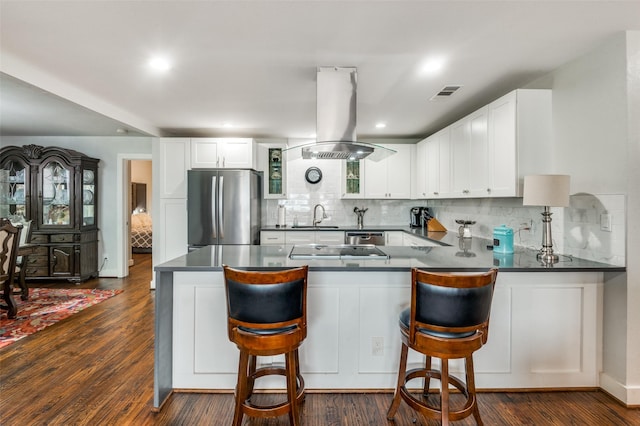 kitchen featuring visible vents, a sink, dark countertops, freestanding refrigerator, and island range hood