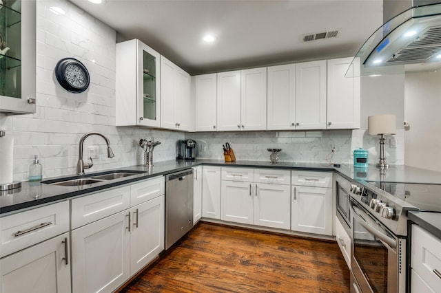 kitchen featuring visible vents, a sink, dark countertops, stainless steel appliances, and wall chimney range hood