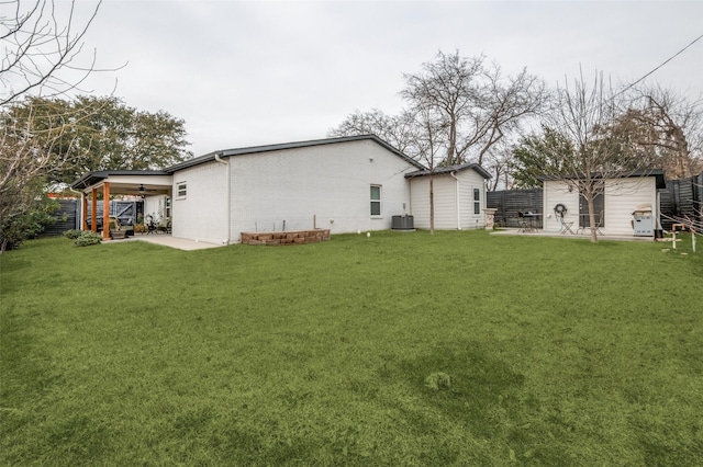 back of house with a yard, brick siding, an outdoor structure, and a ceiling fan